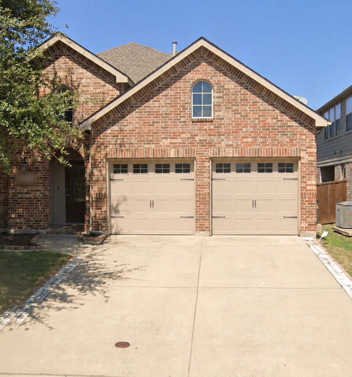 Two sandstone carriage-house short-panel garage doors with window tops on a red brick home