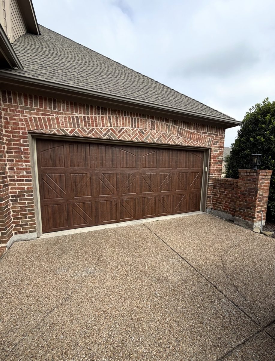 Stamped carriage-house garage door in a dark wood finish on a red brick home