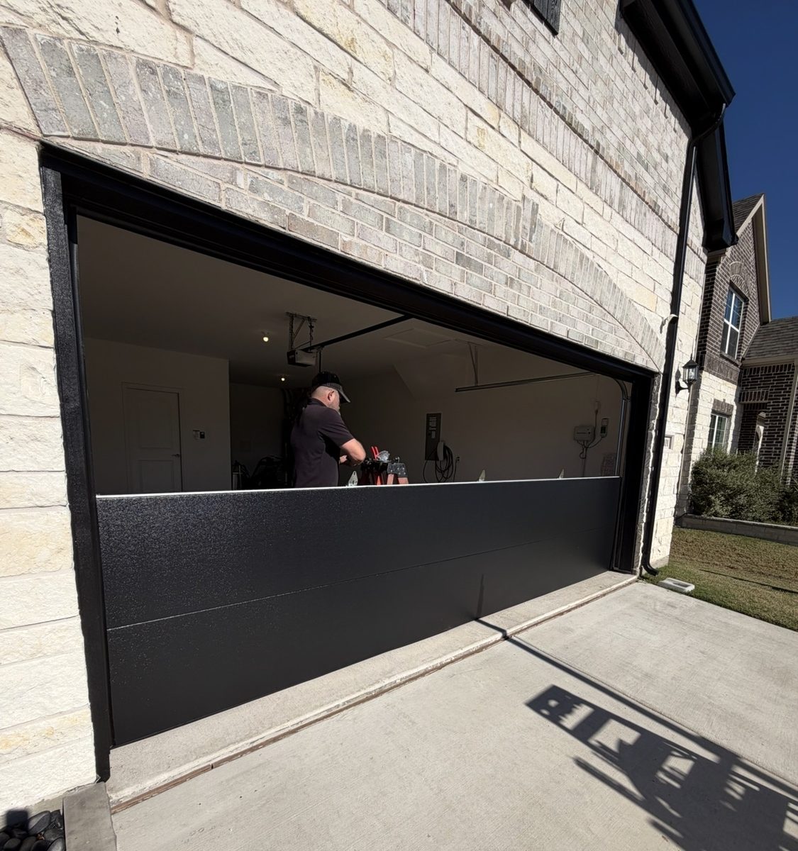 Technician installing a black flush-panel garage door, door partly raised