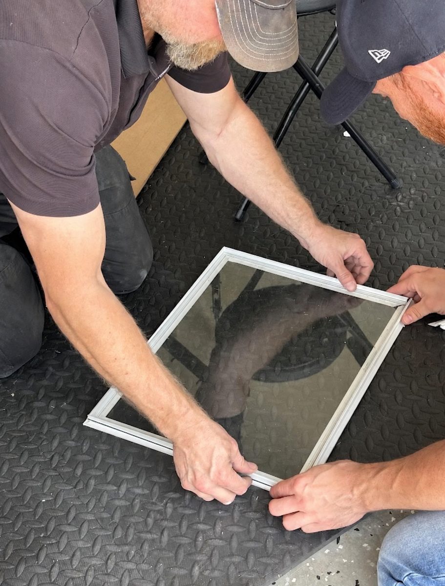 Two technicians seating glass into a garage door window frame