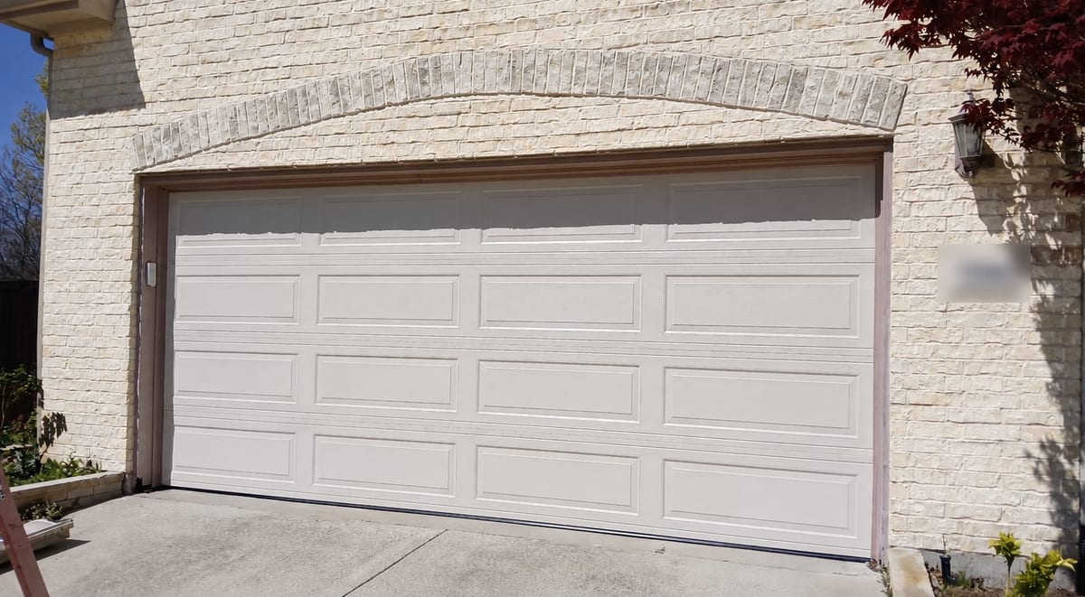 White raised long-panel garage door installed on a light stone home