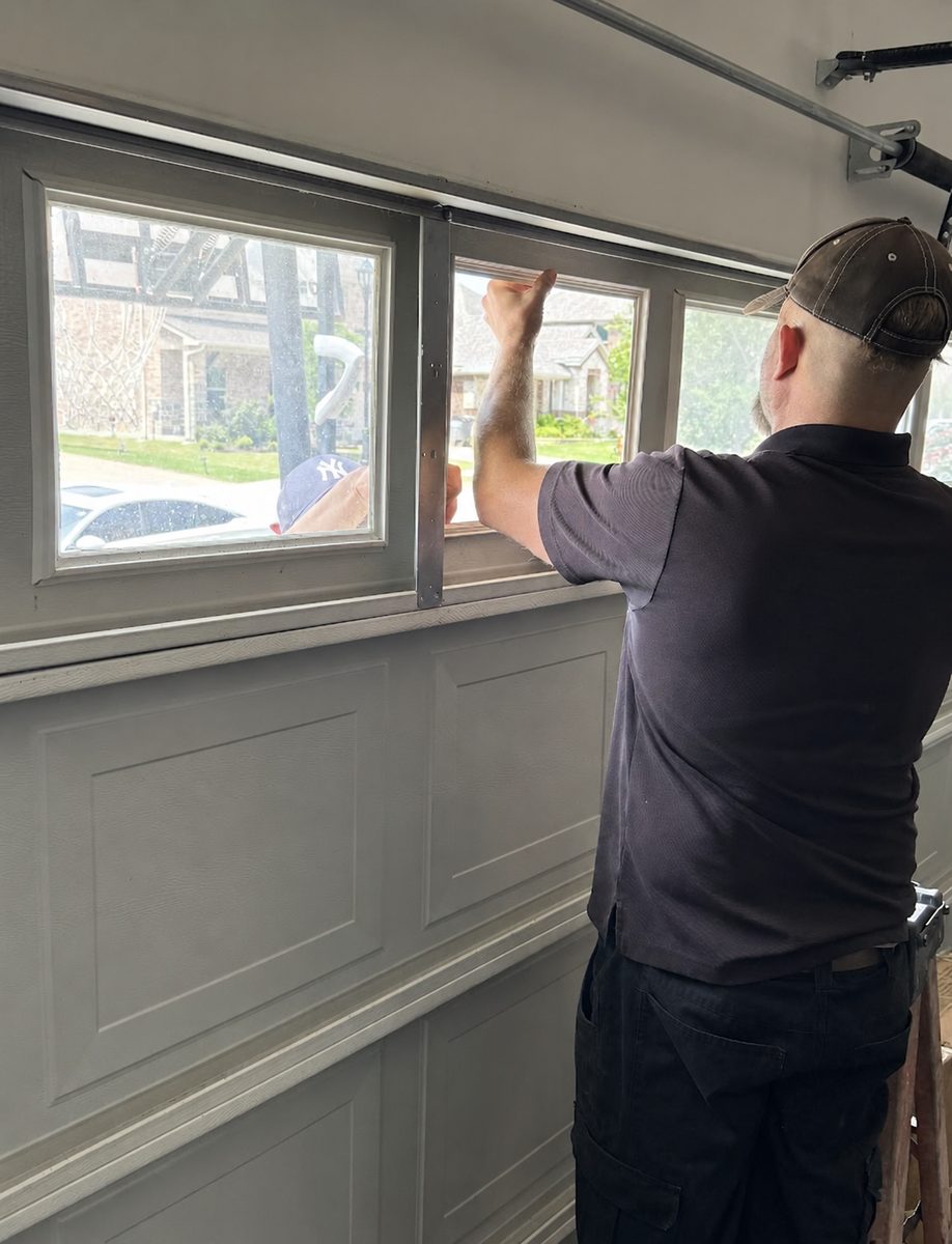 Technician fitting a replacement window insert into a garage door section