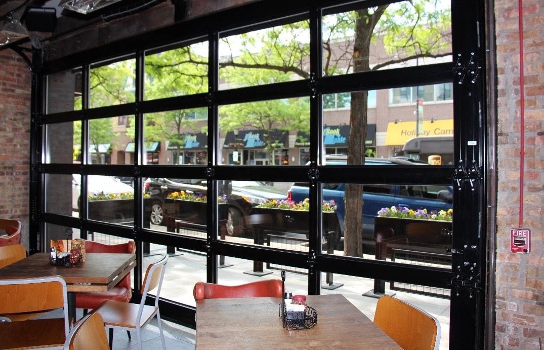 Full-view glass garage door opening a restaurant dining room onto the street